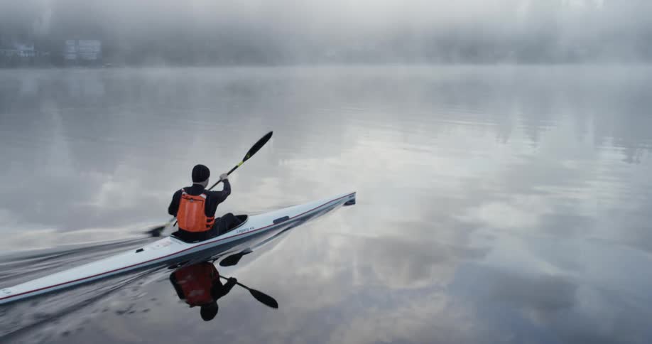 A man is rowing in a canoe on a foggy day