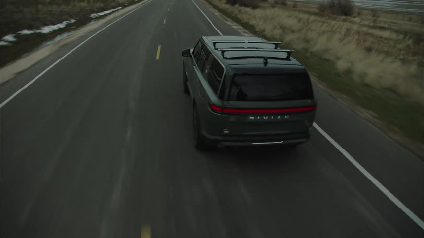 Grey rivian suv traveling a rural highway towards mountains
