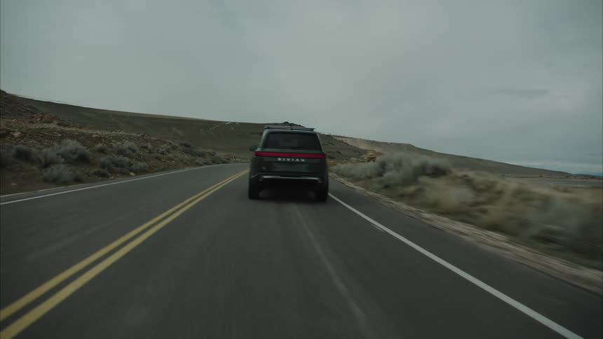 Suv driving on a road through grass lands towards the mountains