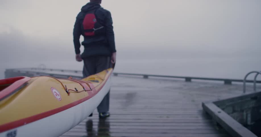A person is carrying a canoe to the water on a foggy day