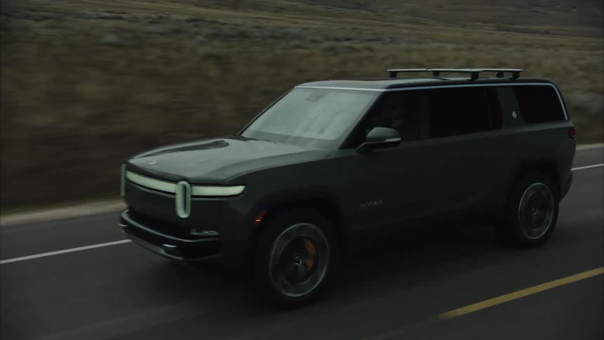 Rivian electric suv driving on rural road alongside snow covered mounains