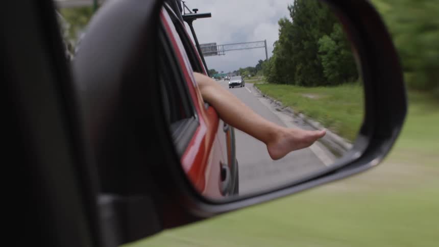 A person riding in a car with their bare leg hanging out the window