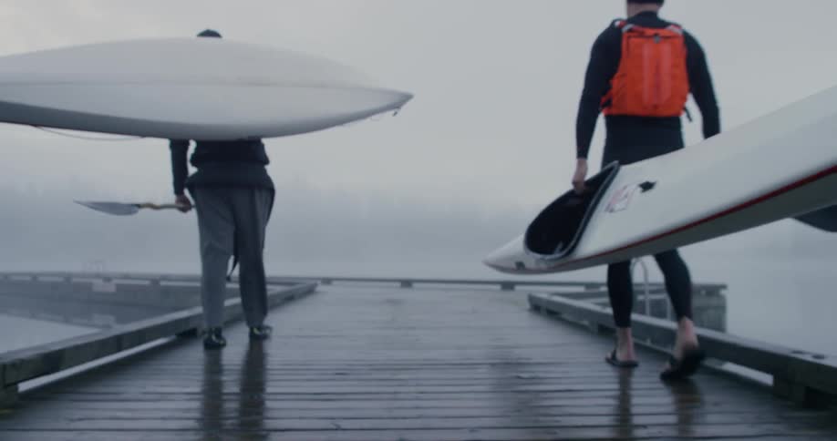 Two people walk to the water with canoes