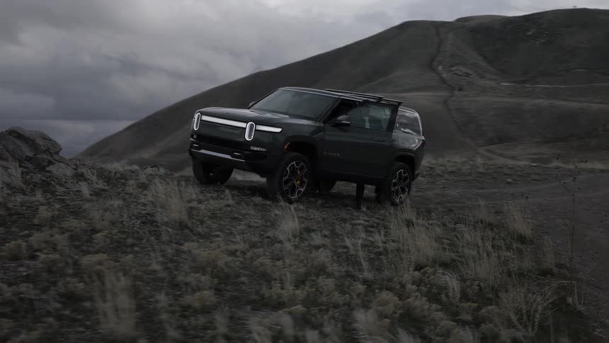 Man parks a vehicle near a hill overlooking the coast on a cloudy day then exits to stand looking at the scene