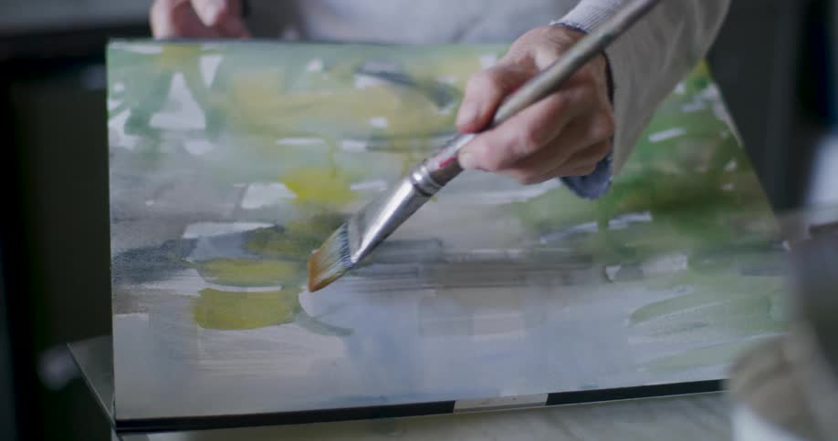 A person is standing indoors and painting a picture