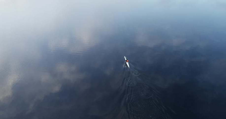The clouds are reflected in water as a kayaker paddles across it