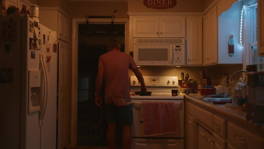 Man cooking at home adds an egg to a skillet on the stove top