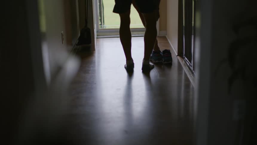 A man walks down a hallway and puts on his shoes
