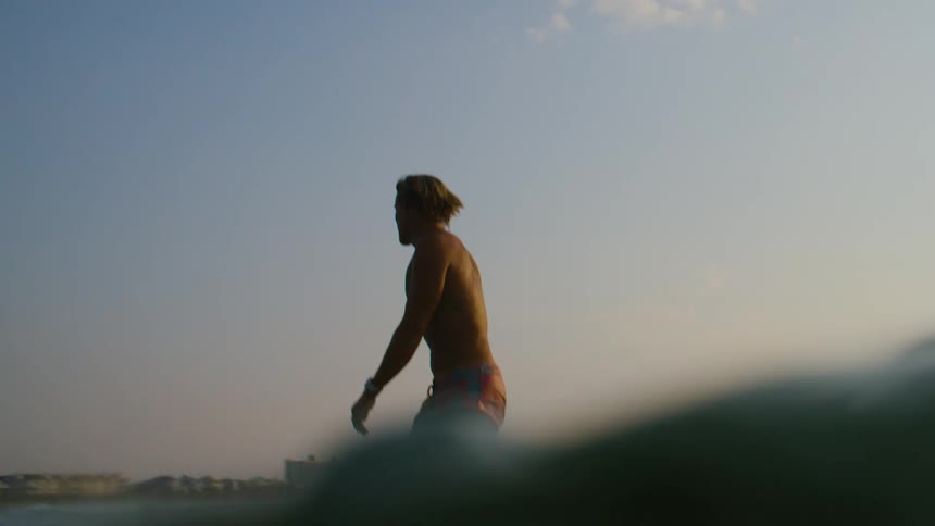 Male is surfing on waves in the ocean at dusk