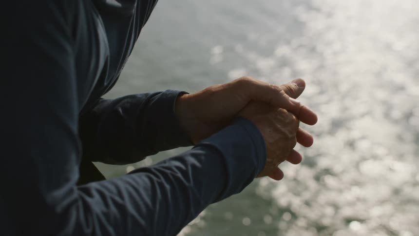 A man with folded hands leans on a railing looking out over a large body of water