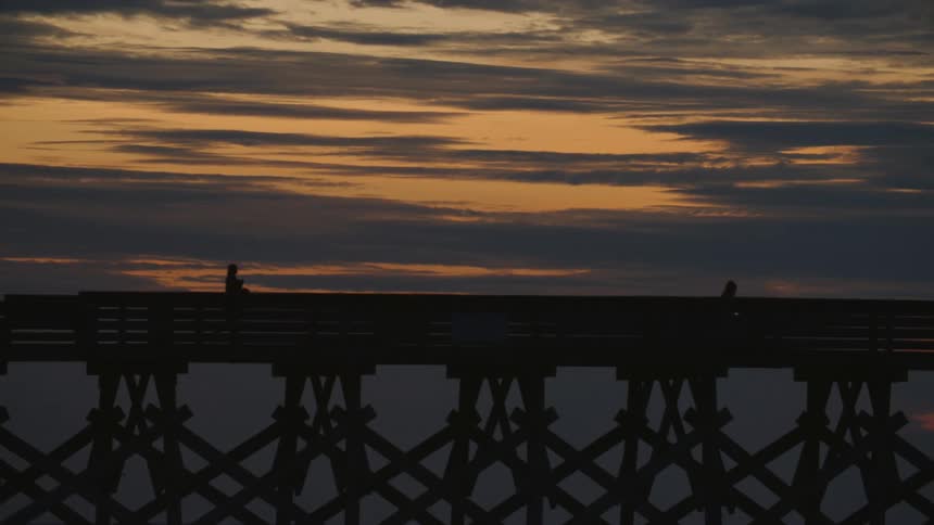 People are walking on the pier at sunrise