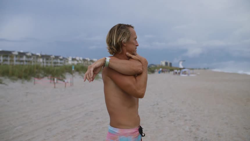A man is stretching his arms on the sandy beach