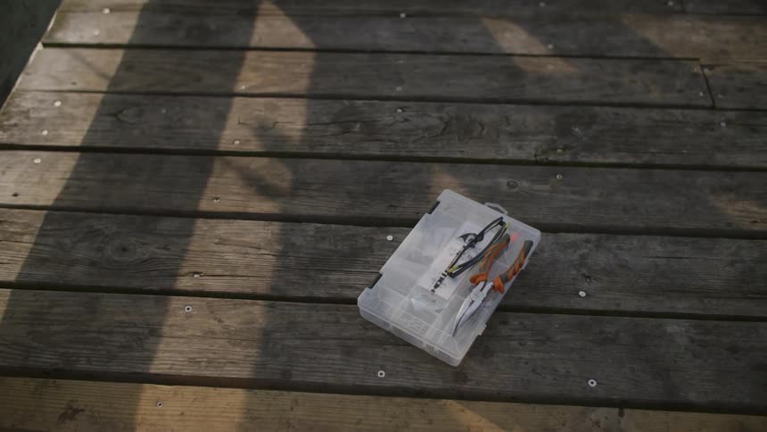 Fishing pliers laying on plastic tackle box on a wooden dock with slats
