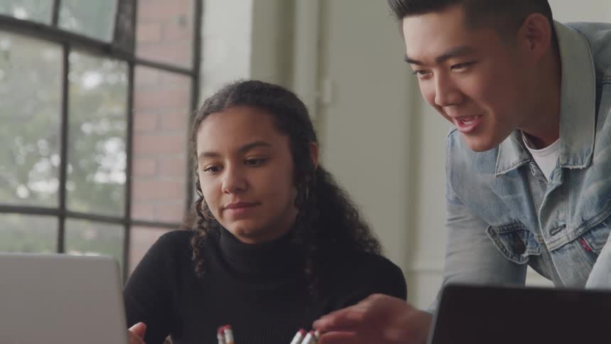 Two workers look at a laptop and talk