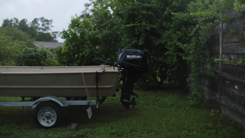 Motorboat and trailer stand near a wooden fence in a residential area during the daytime