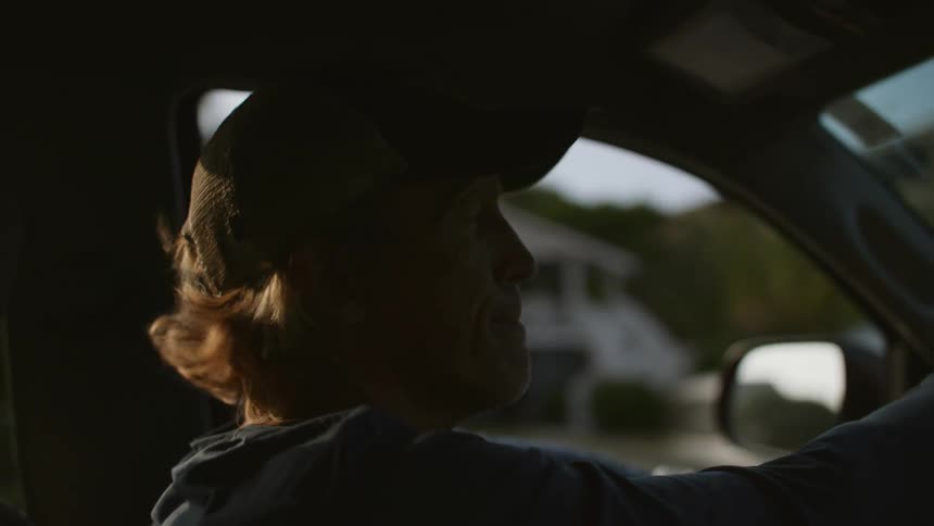 A man wearing a hat is driving a car through the suburbs