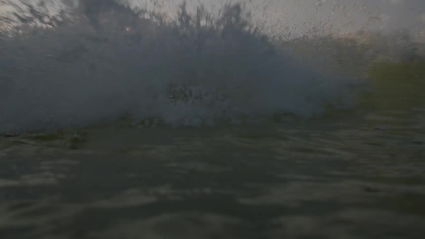 A wave crashes dramatically as sunlight breaks through clouds scattering golden reflections across the oceans surface