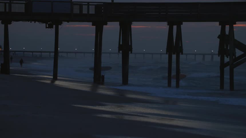 Two people walk into the ocean with their surfboards in hand at dusk