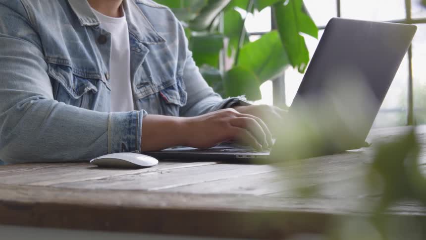 A man sits at a wooden desk while typing on a laptop computer