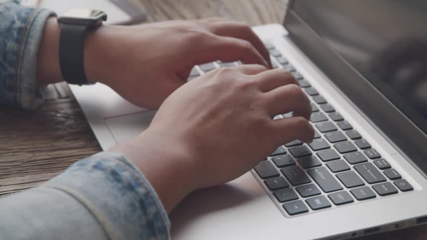 While typing on a laptop a person is wearing a watch