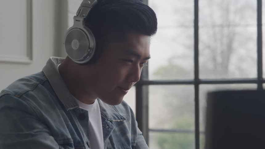 Sitting at a computer desk a teenager is wearing headphones