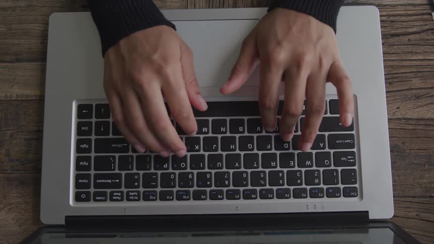 View looking down at a mans hands typing on the keyboard of a laptop computer
