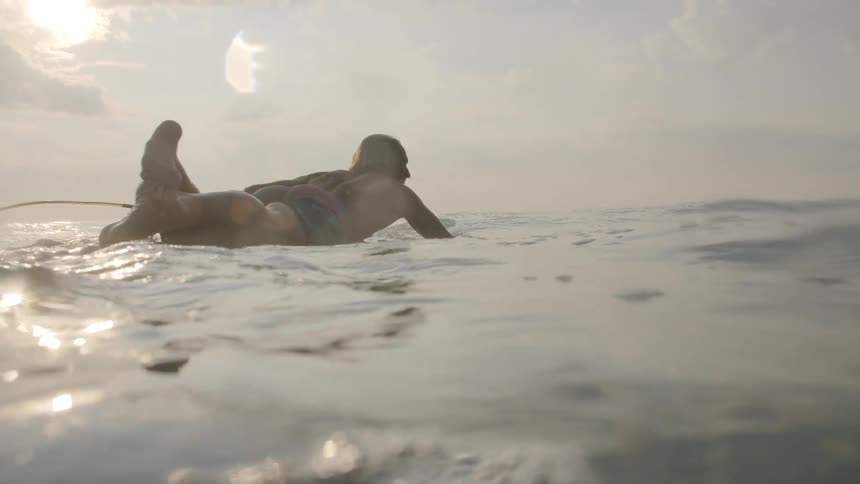 Man lying on his surfboard paddling across the water