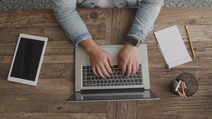 A person is typing on their laptop and sitting at a desk