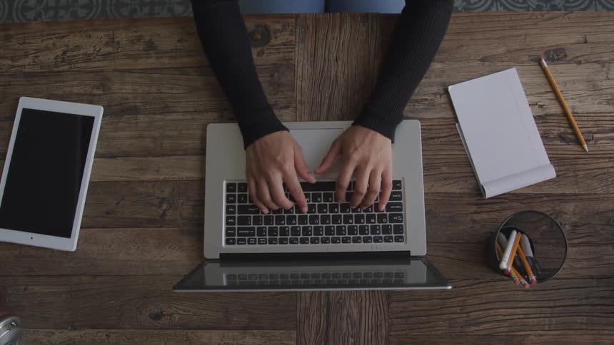A woman is typing on her laptop at the desk