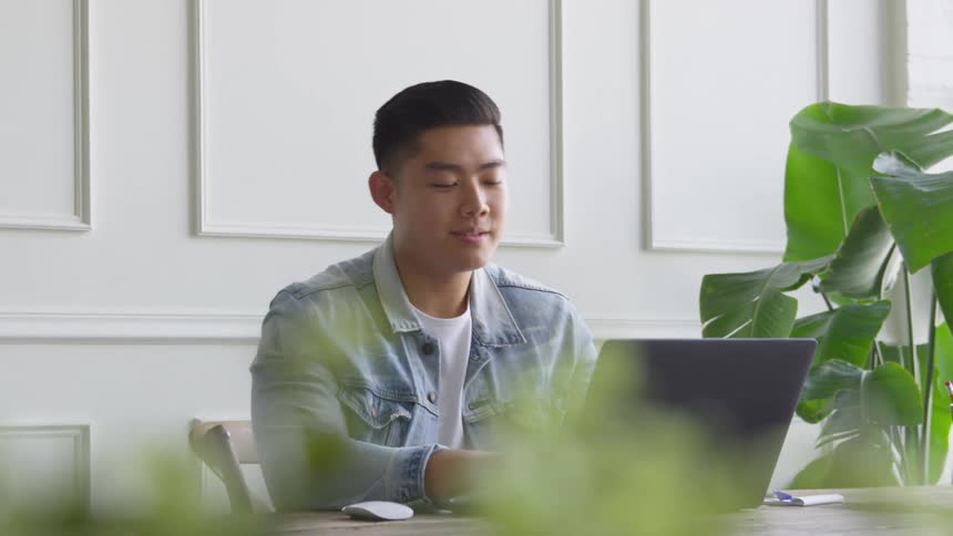 A male is smiling and typing on his laptop