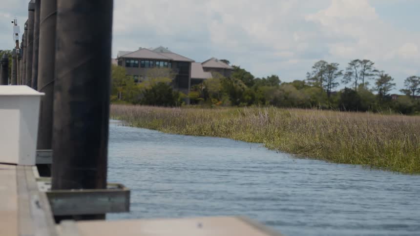Water flows between the dock and the field bordering a multistory building on a cloudy day