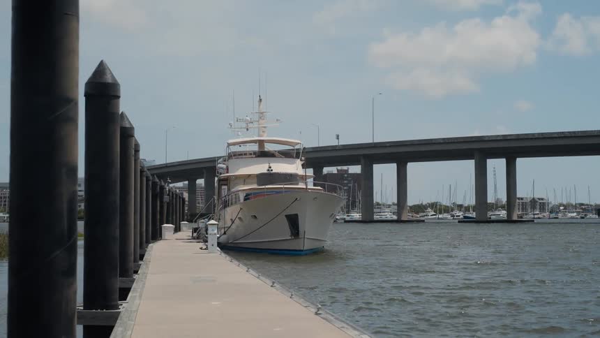 Man stands near the yacht docked on the opposite side of a bridge from a marina on a cloudy day