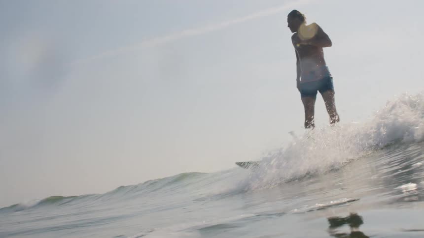 Surfer stands on his surfboard and rides a wave into shore