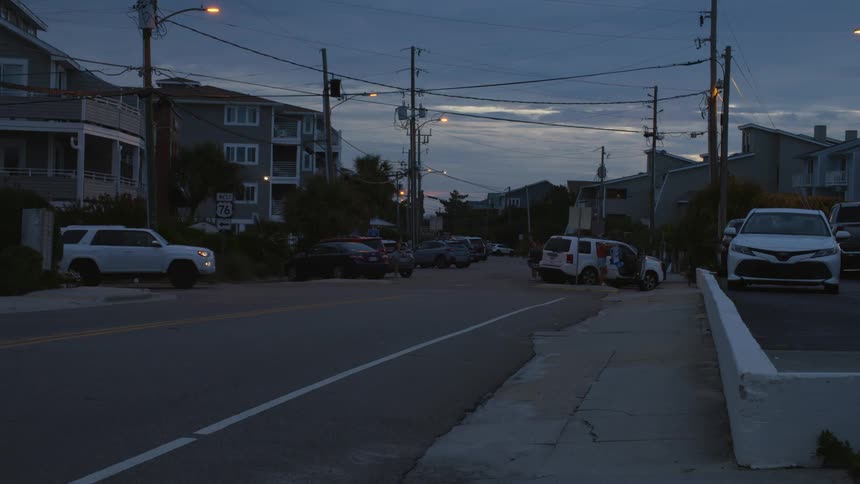 There are people riding bikes down the street and there are cars parked everywhere