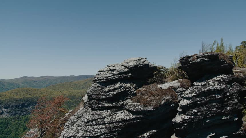 A rocky outcrop overlooks a forested valley under a clear blue sky