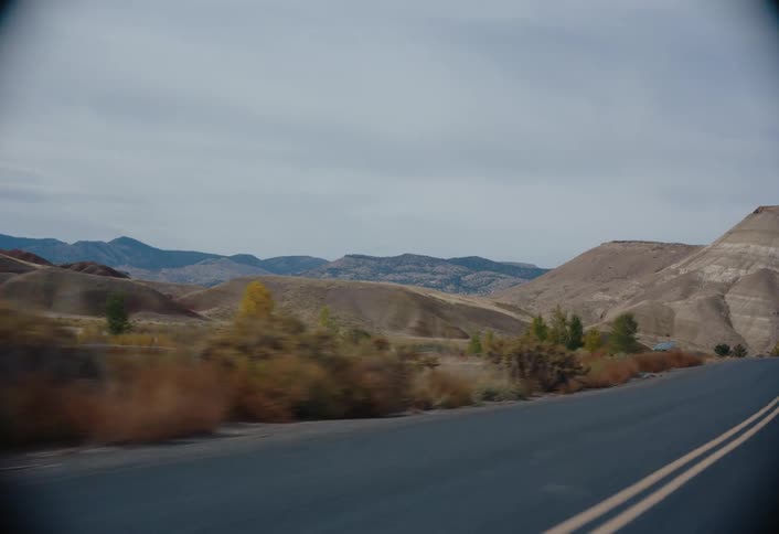 A paved road with double yellow lines curves through a landscape of rolling hills under a cloudy sky
