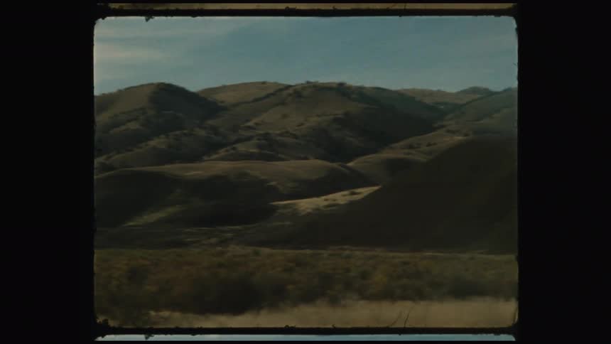 A landscape of rolling hills under a cloudy sky with a dry grassy field in the foreground