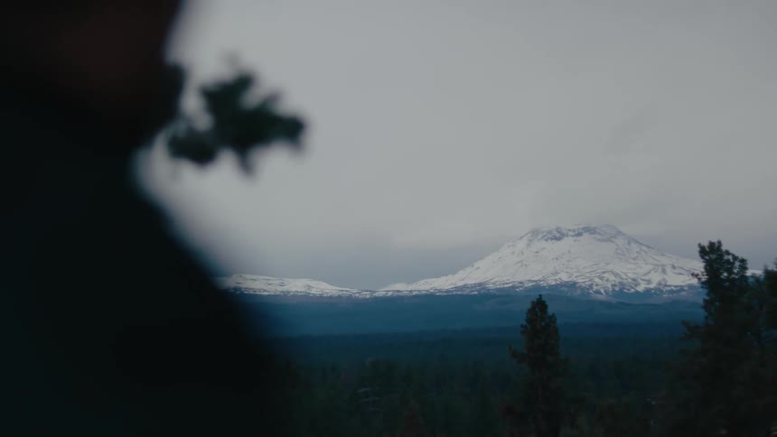 A snow capped mountain rises majestically in the distance partially obscured by the silhouette of a man standing in the foreground