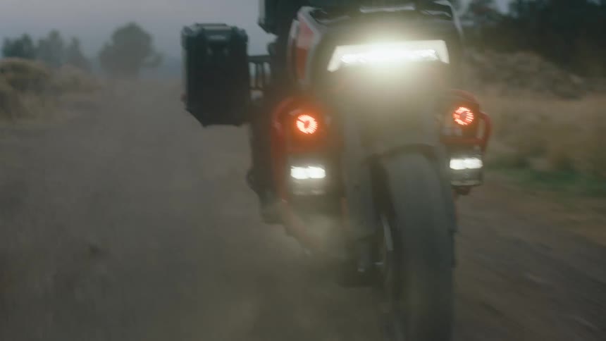 A motorcycle with a bright headlight driving on a dirt road in a foggy environment