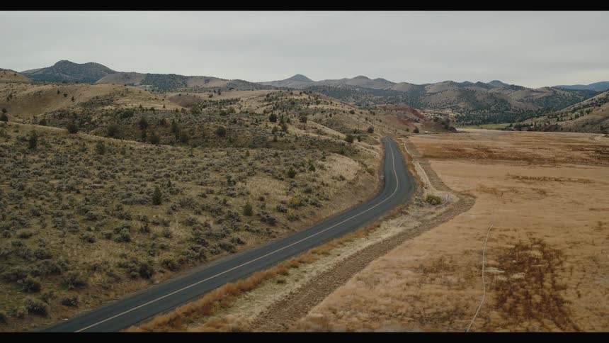A paved road curves through a dry hilly landscape under an overcast sky