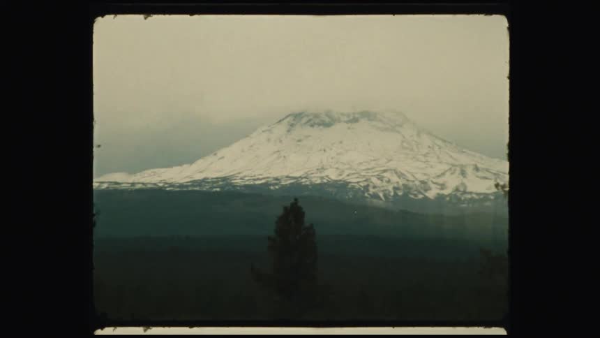 A snow capped mountain partially obscured by mist or clouds with a dark foreground featuring silhouetted trees