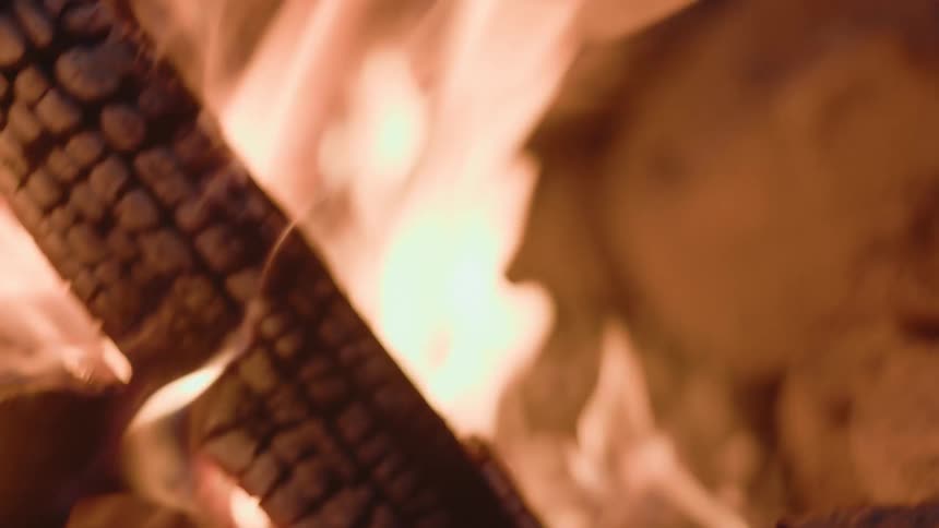 Flames of a campfire glow in the darkness as the wood burns