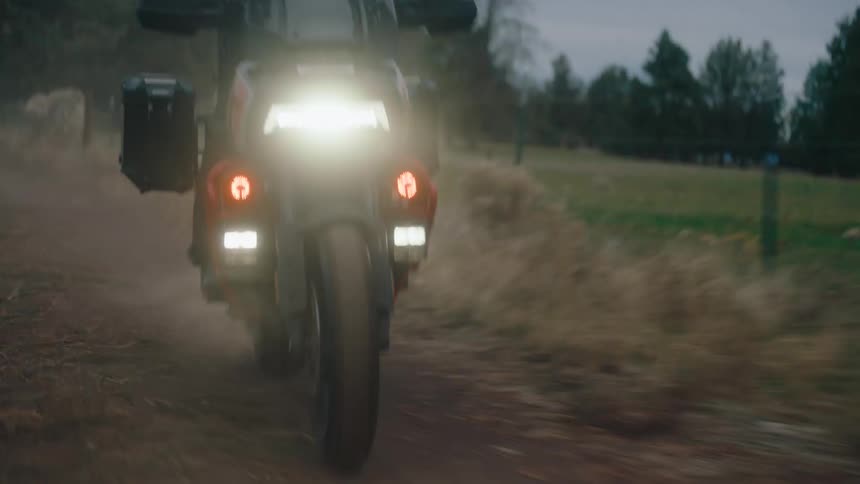 A man is riding a motorcycle on a dirt road in the evening