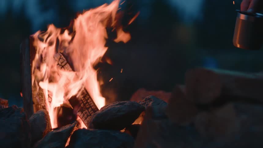 A man has a coffee cup in his hand as he sits by a campfire
