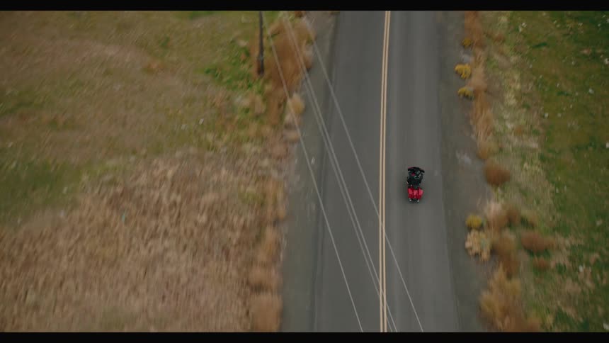 Motorcycle rider travels down a road past mountains and through grassy areas