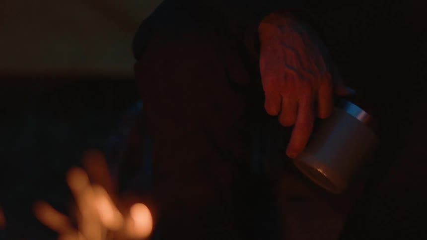 A man sits by the fire with a cup