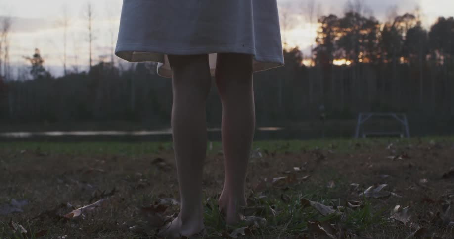 Barefooted woman wearing a skirt standing outdoors at sunset as seen from her thighs down