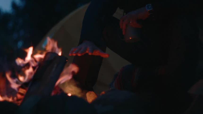 A man is warming his hands on the campfire