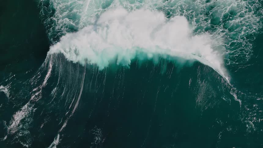 A large wave breaking its white foam contrasting sharply with the deep green and blue tones of the ocean