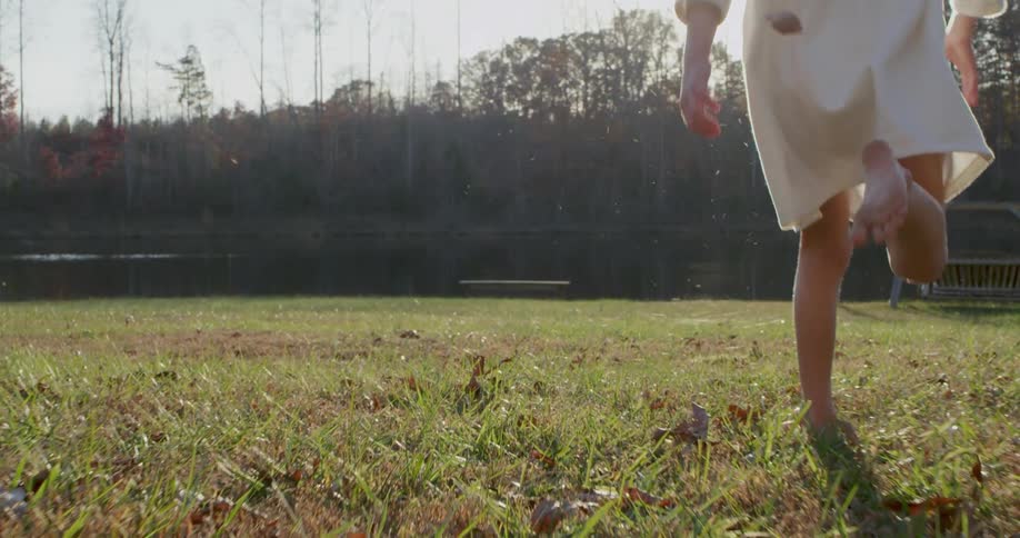 A barefoot girl runs through grass on a sunny day